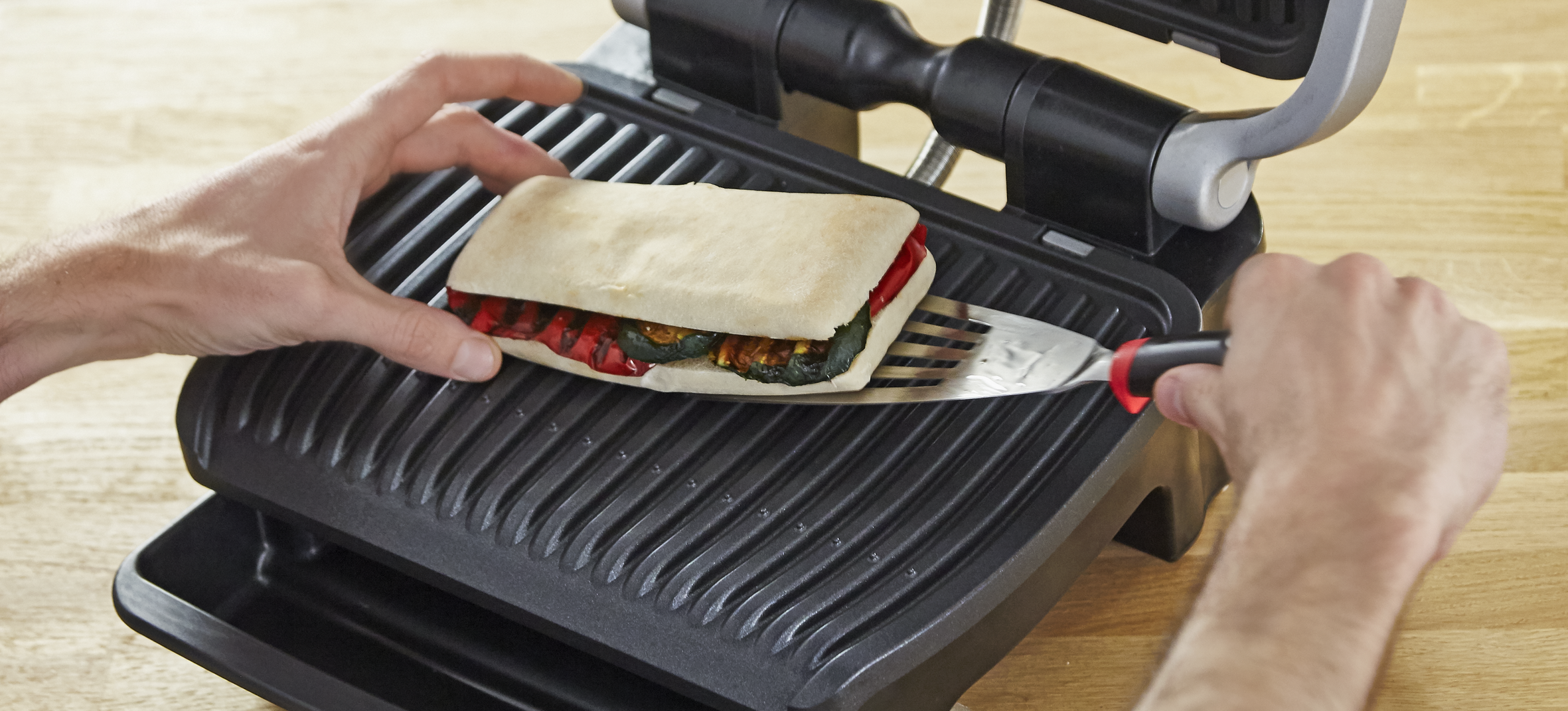 Person placing a sandwich on a black panini press with a metal spatula.