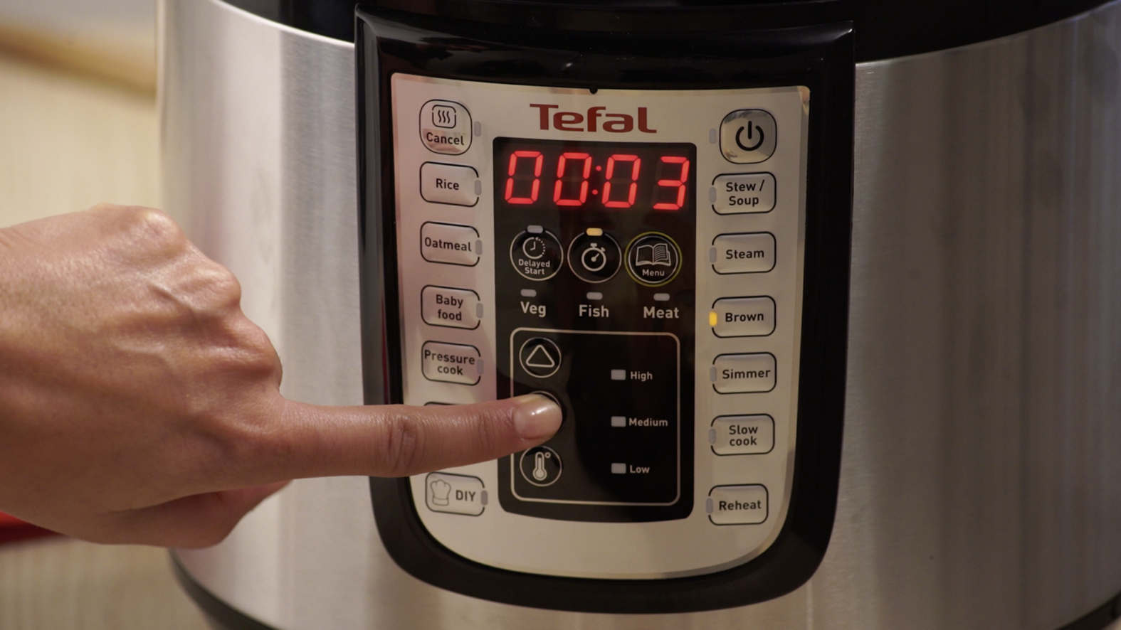 De hand van een persoon die op een knop drukt op een Tefal snelkookpan. Het display toont 00:03.