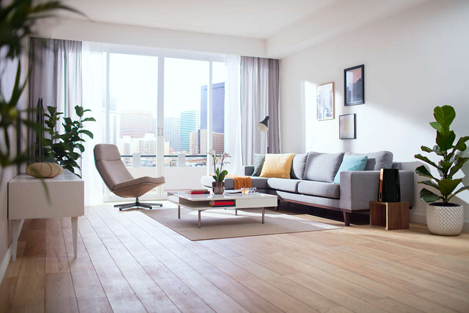 Ein modernes Wohnzimmer mit hellem Holzboden, einem grauen Sofa und einem großen Fenster.