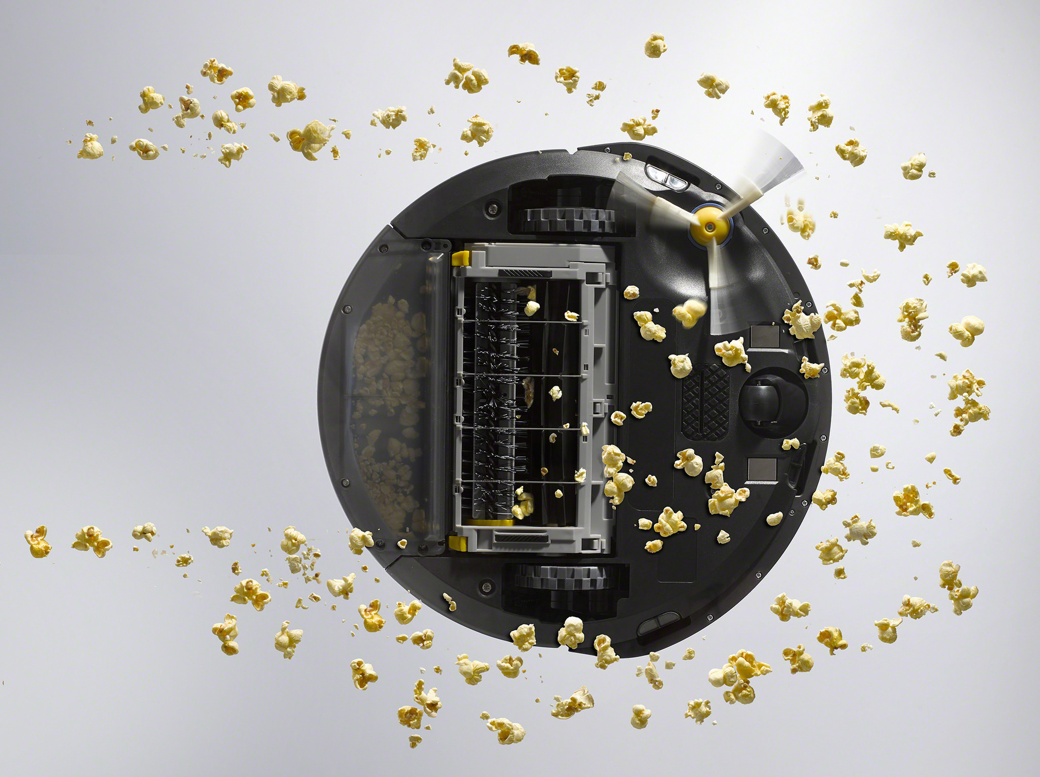 Roboter-Staubsauger, Draufsicht, umgeben von Popcorn. Reinigungsaktion visualisiert.