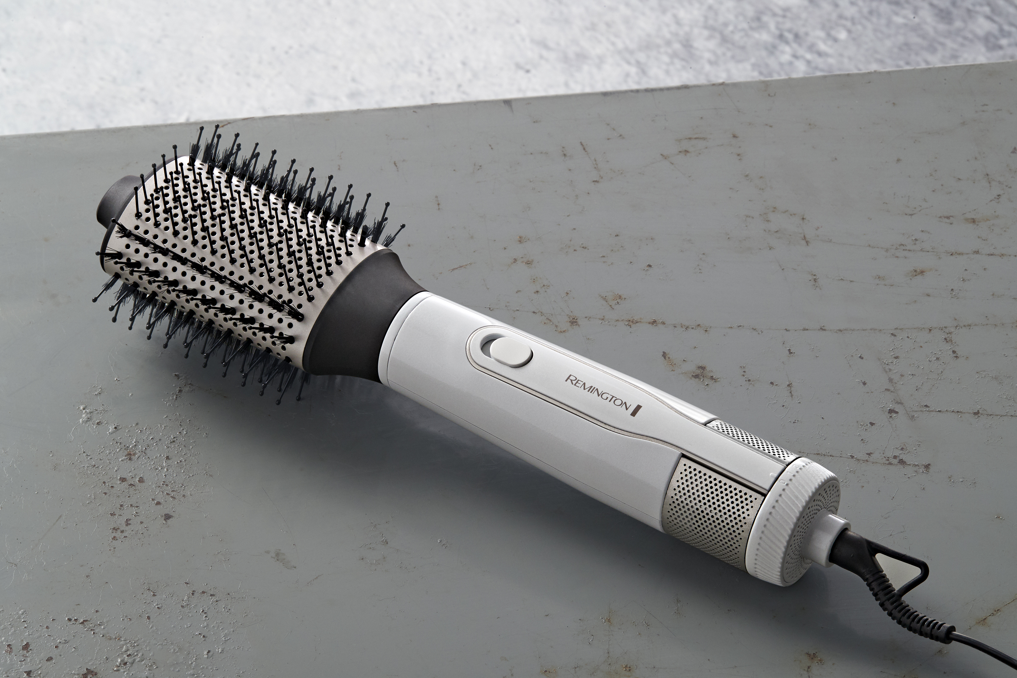 Eine weiß-schwarze Haarbürste auf einer metallisch-grauen Oberfläche, mit schwarzem Kabel.