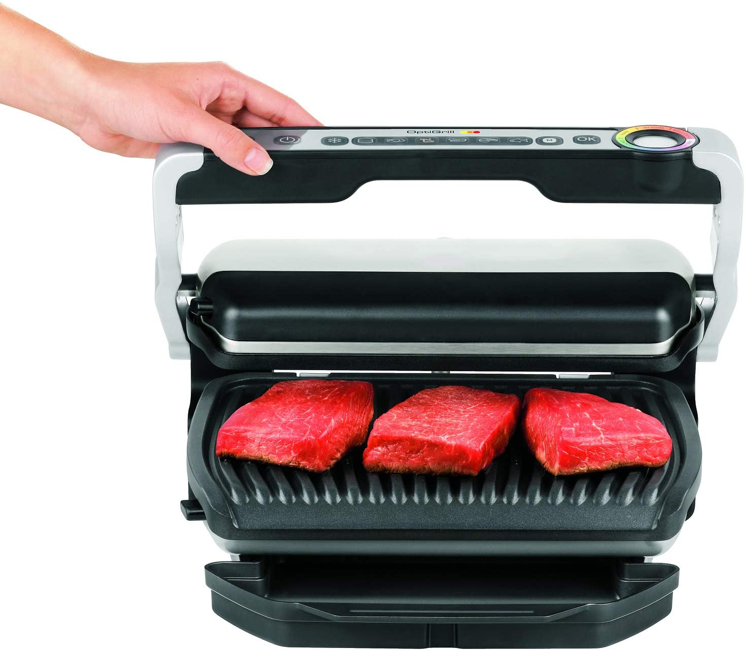 Griglia elettrica con tre pezzi di carne cruda. Mano che aziona i comandi. Superficie di cottura pulita.