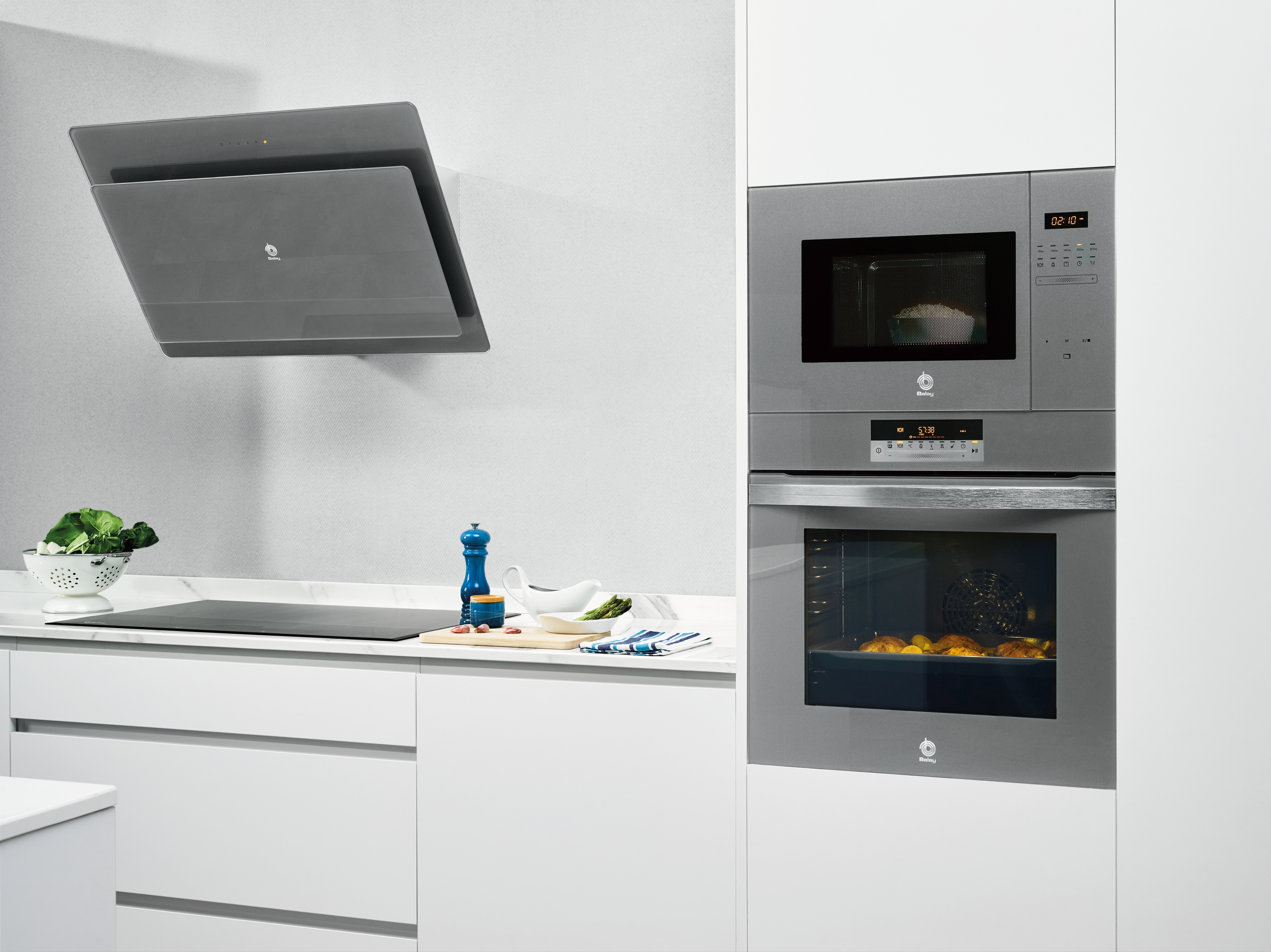 Electrodomésticos de cocina modernos, incluyendo campana, microondas, horno y vitrocerámica, sobre fondo blanco.