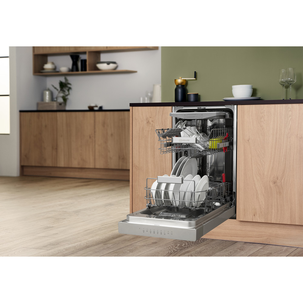 Eine Spülmaschine ist geöffnet, mit Tellern und Gläsern. Holzschränke im Hintergrund.