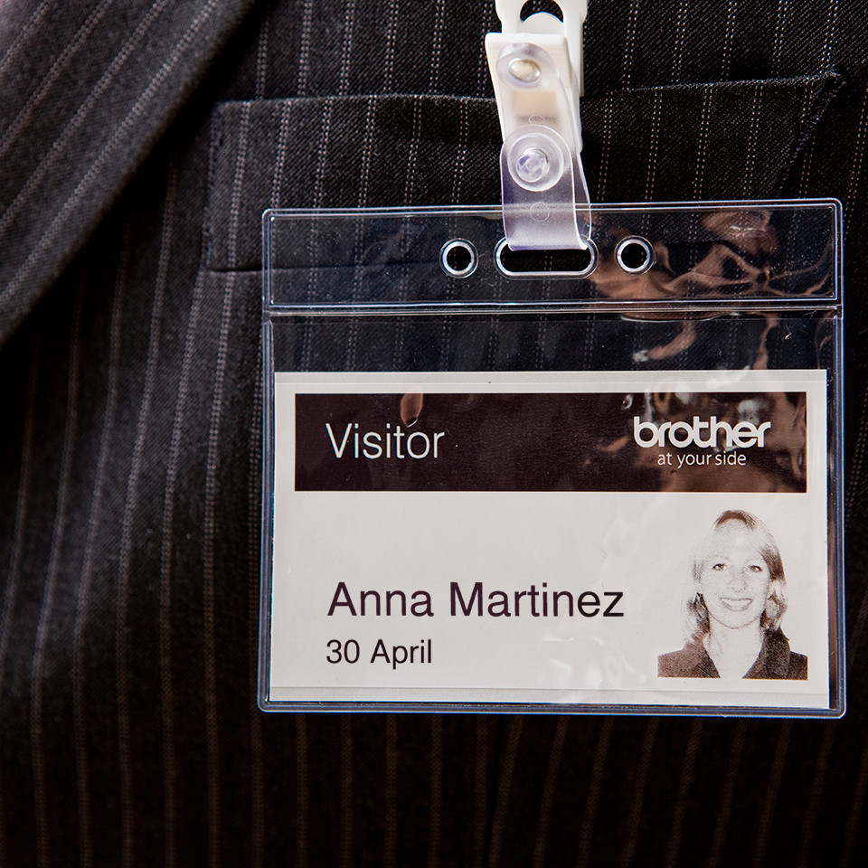 Badge de visiteur accroché à une veste de costume, avec nom et photo.