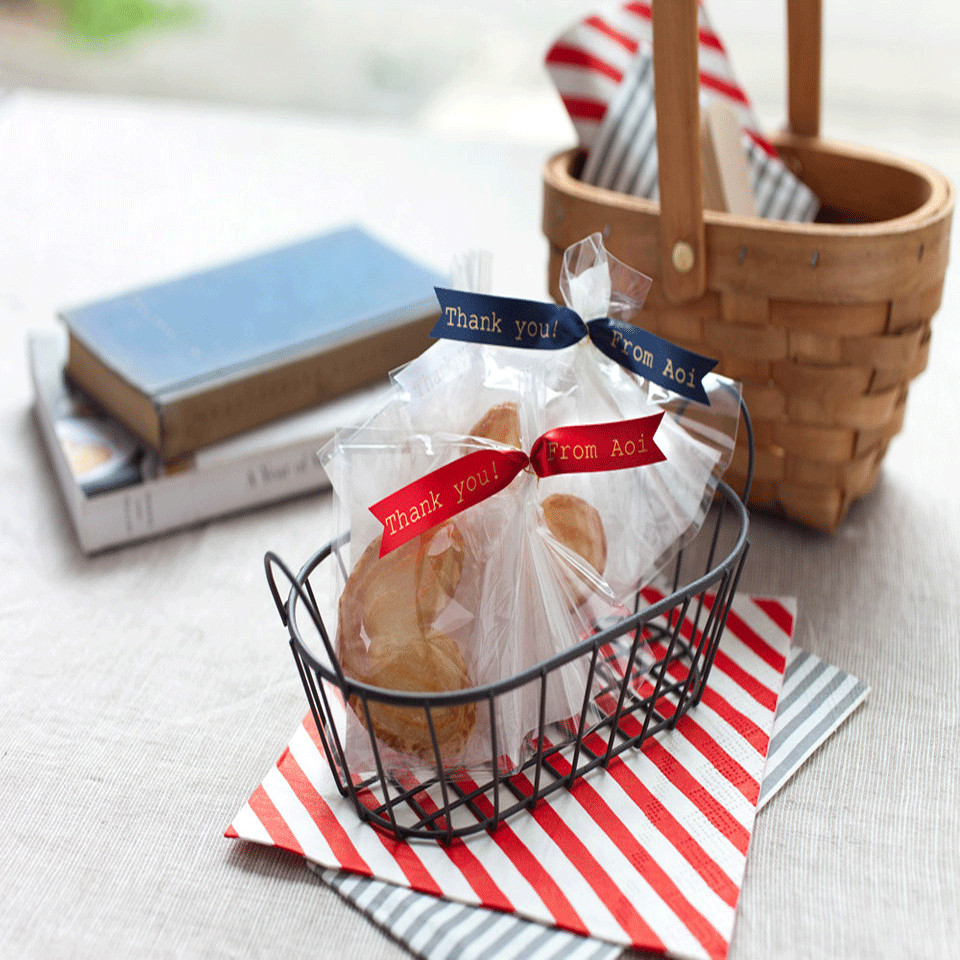 Un petit panier avec des produits de boulangerie, des rubans et un livre sur une table.
