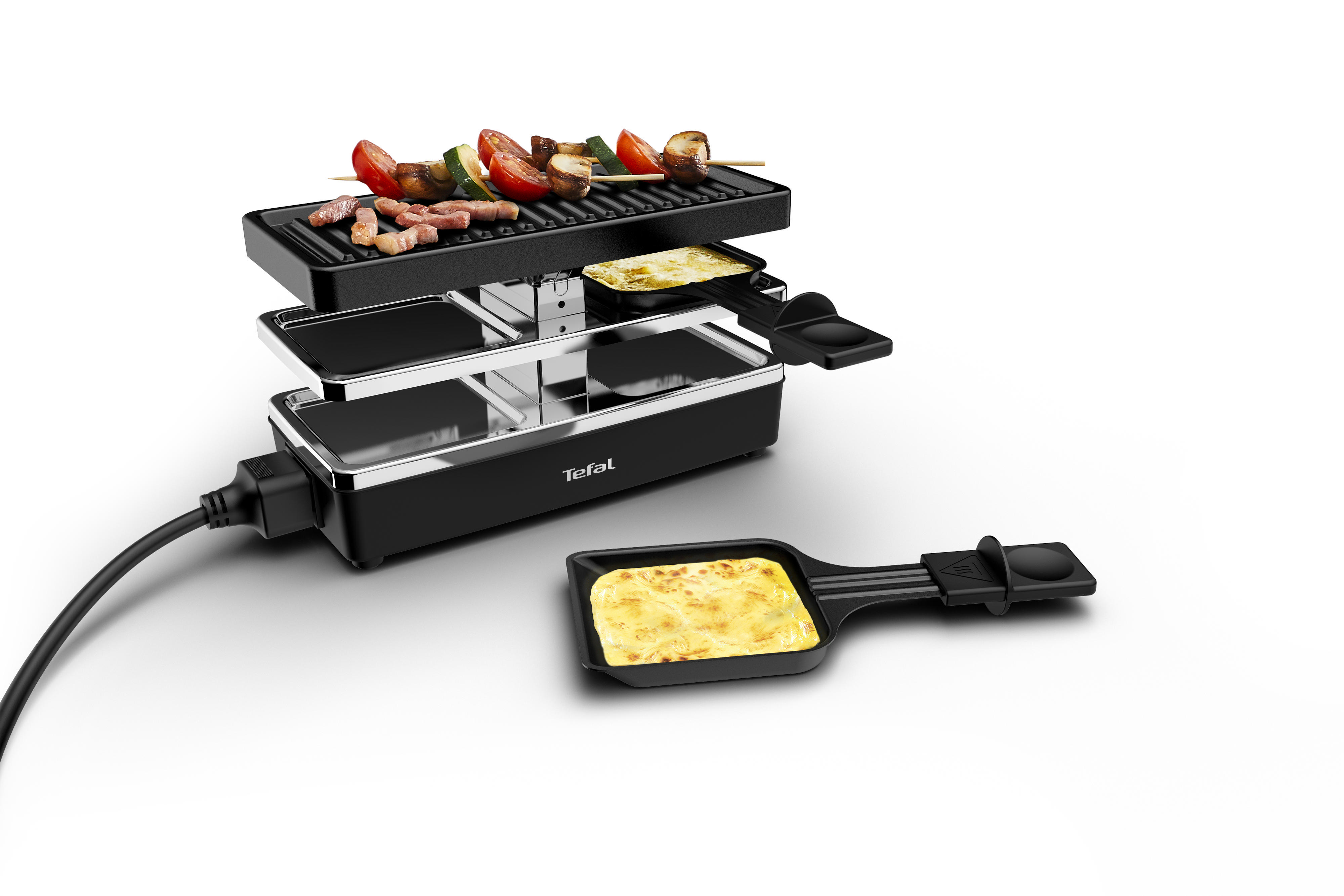 Ein Raclette-Grill mit Essen oben, einem Käseblech und einem schwarzen Netzkabel, weißer Hintergrund.