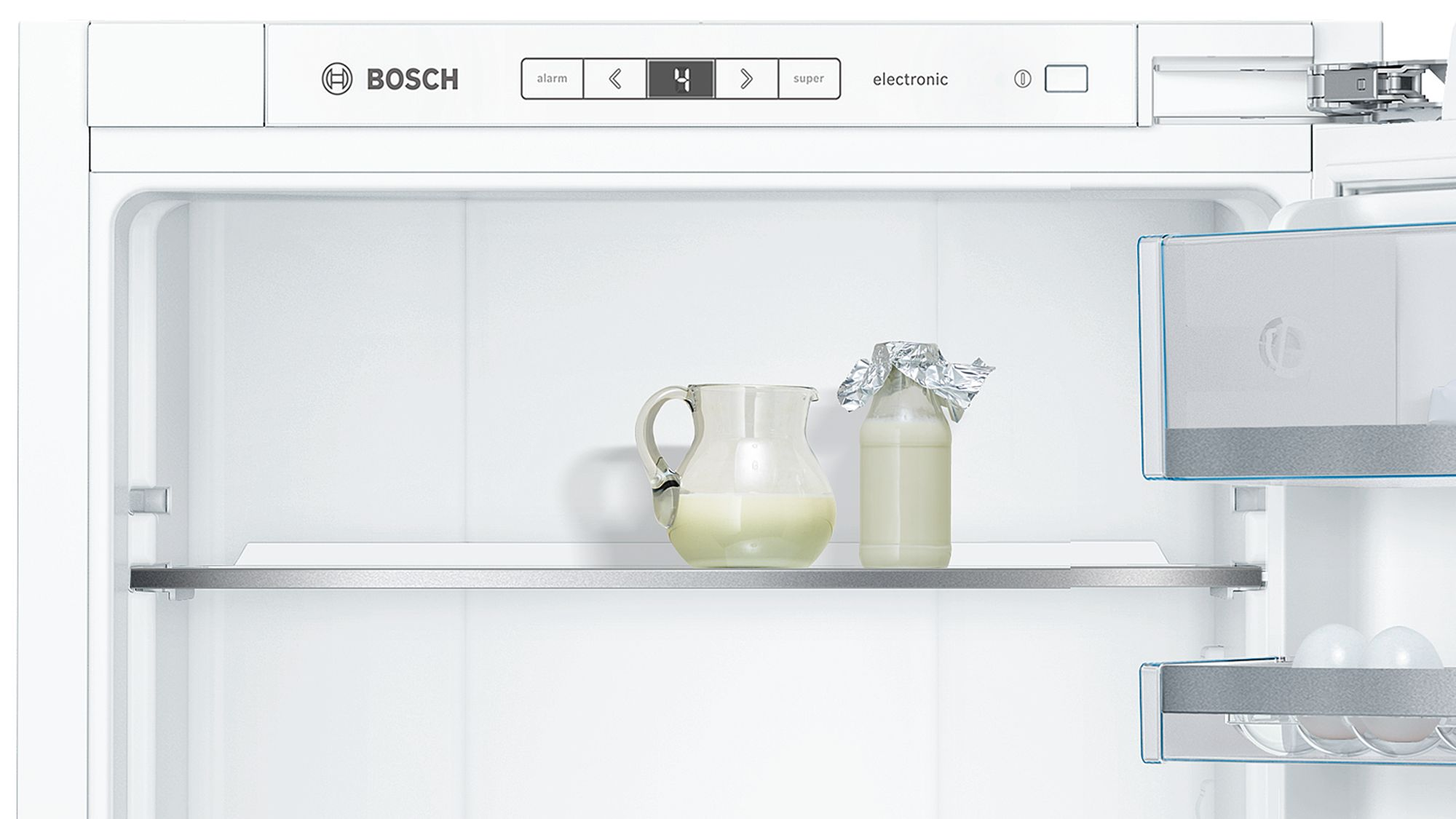 In einem weißen Bosch-Kühlschrank. Milchflaschen und eine Kanne stehen im Regal.