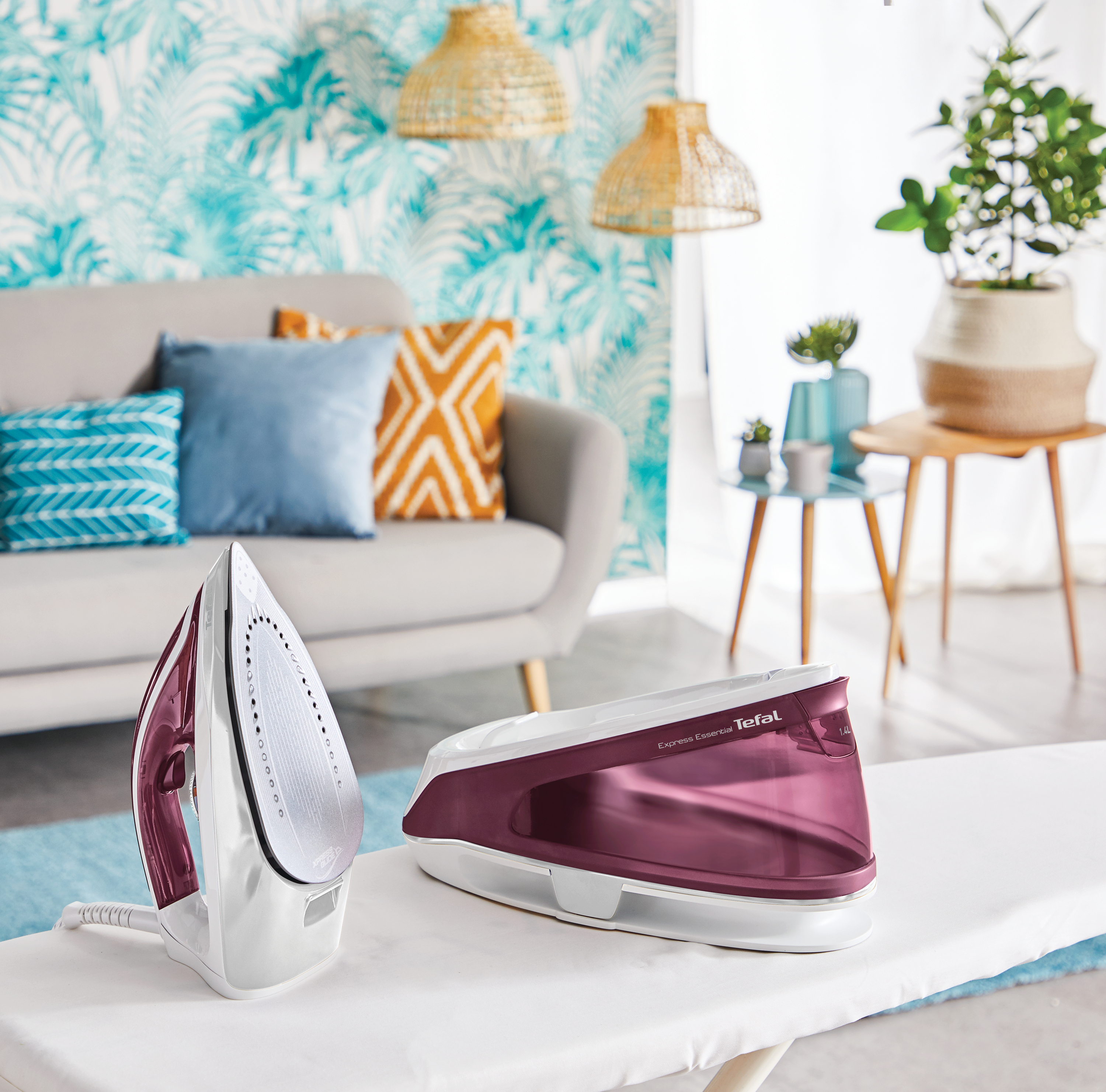 Bügeleisen und Basis mit lila Akzenten. Der Hintergrund zeigt ein Wohnzimmer mit Sofa und Einrichtung.