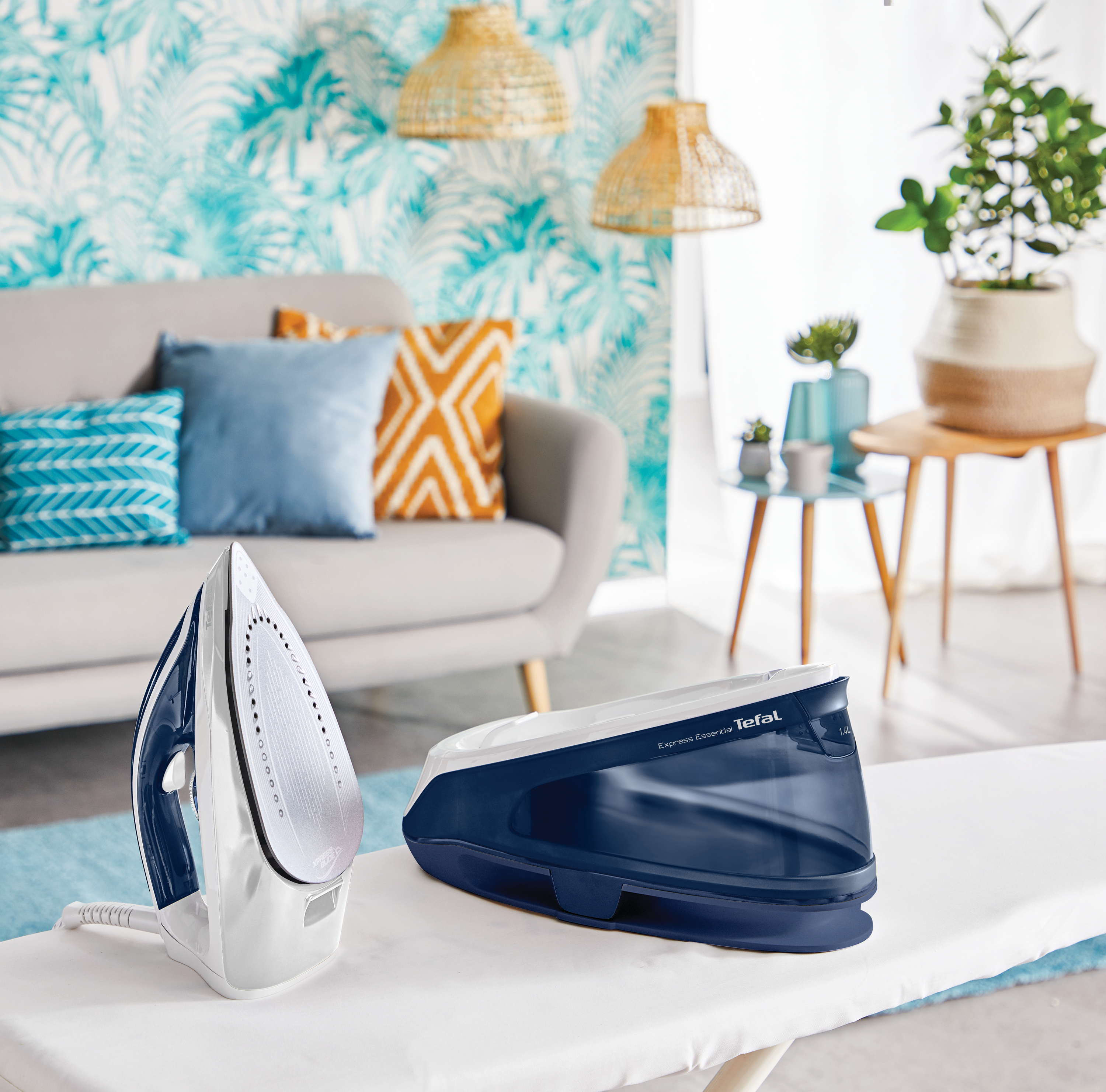 Ein Bügeleisen und seine Basis auf einem Bügelbrett. Blaues und weißes Bügeleisen, blaue Basis. Wohnzimmer im Hintergrund.