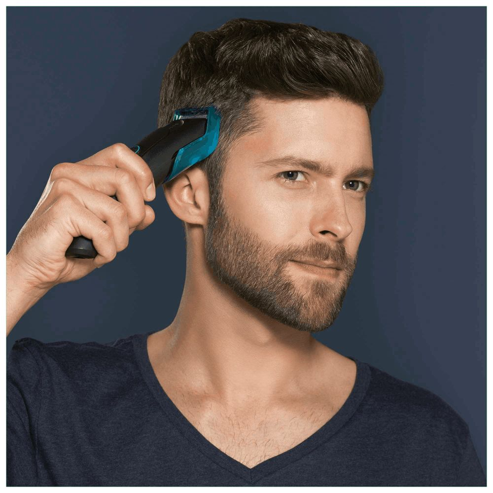 Hombre cortando su cabello con un recortador cerca de la oreja.