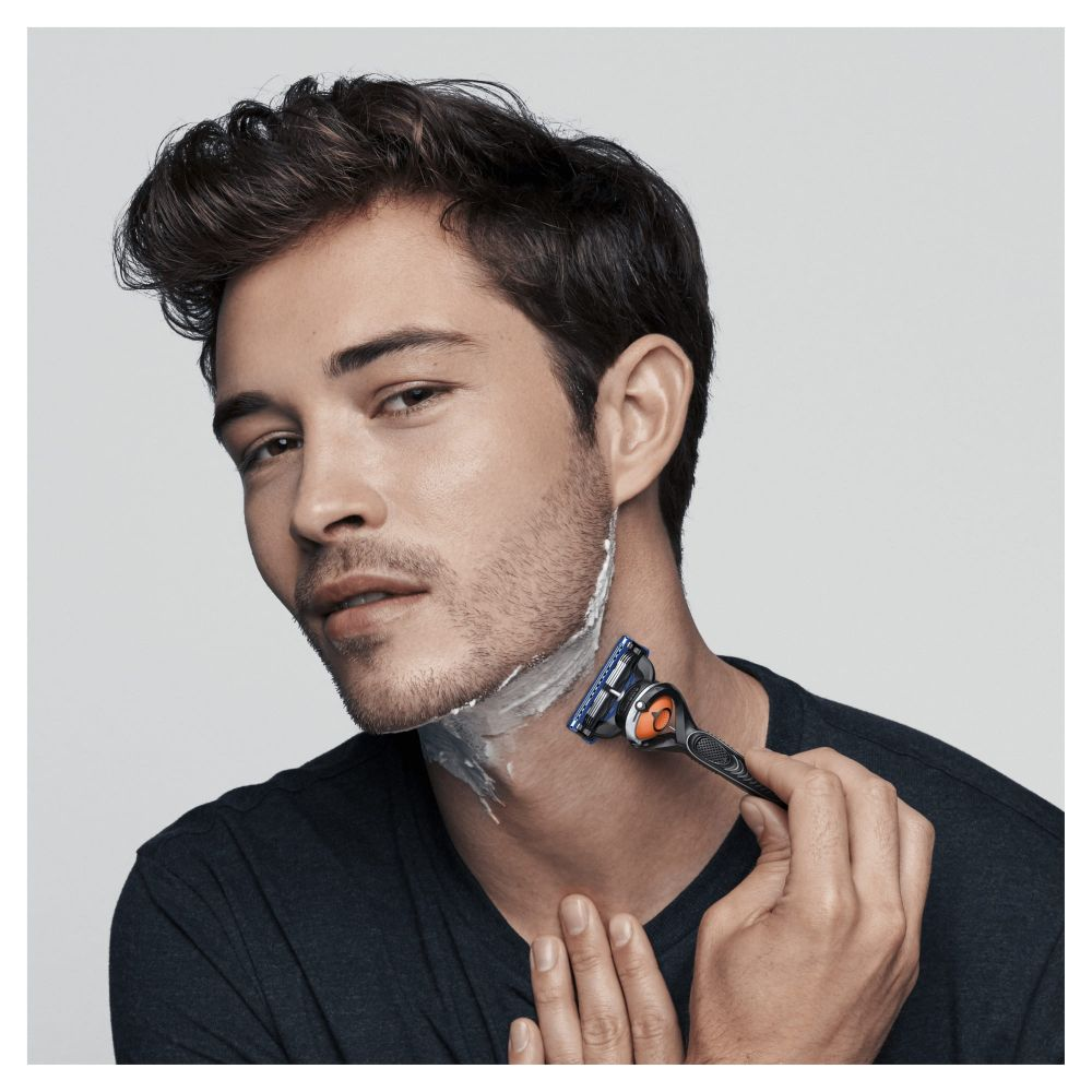 Un hombre afeitándose el cuello con una maquinilla de afeitar azul y naranja, con crema de afeitar en la piel.