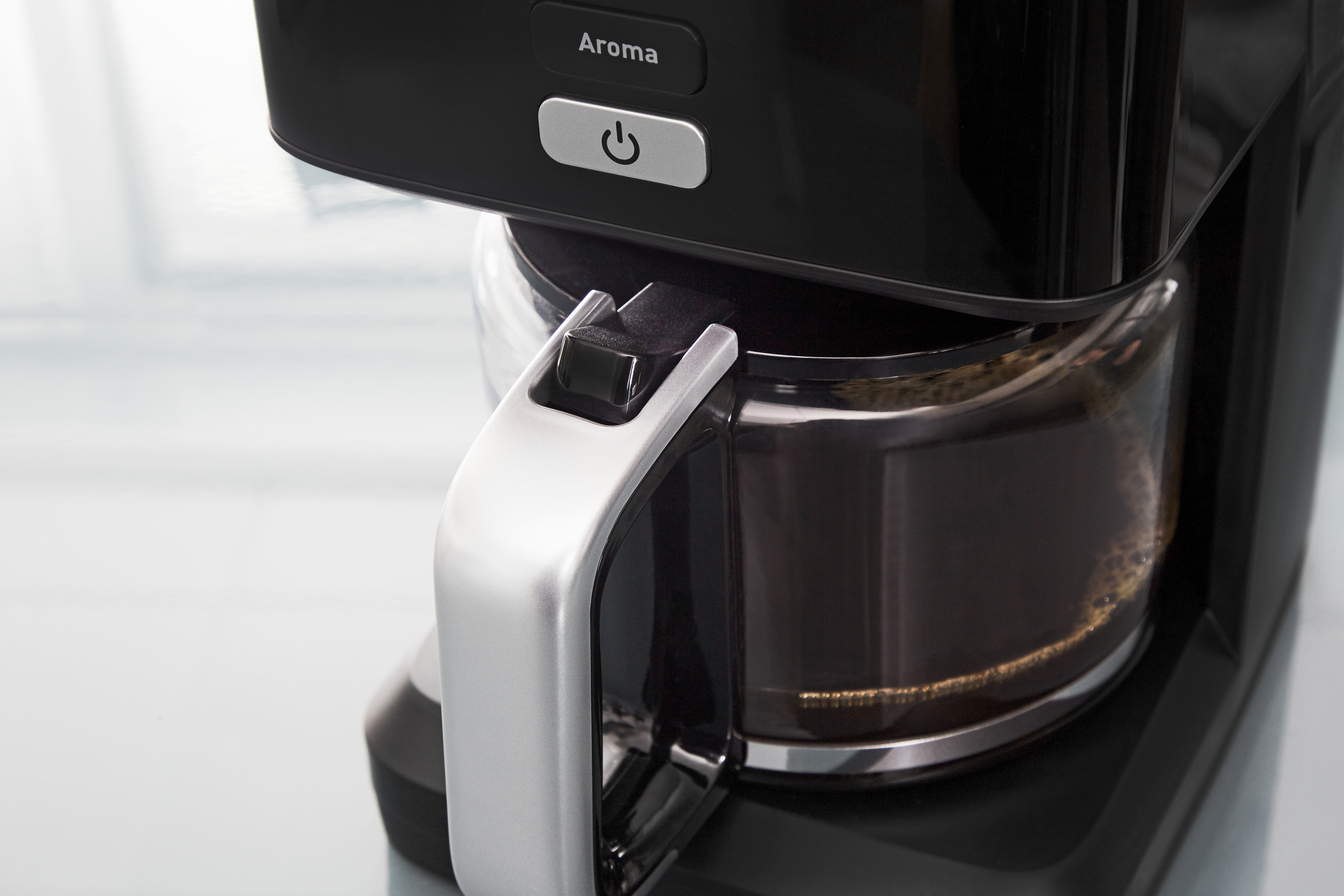 Nahaufnahme eines schwarzen Kaffeeautomaten mit Glaskanne und silberfarbenem Griff.