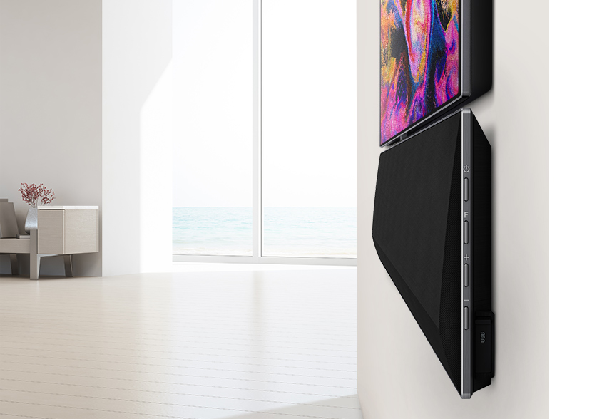 Een zwarte soundbar gemonteerd op een witte muur naast een tv. De tv toont een kleurrijk, abstract beeld.