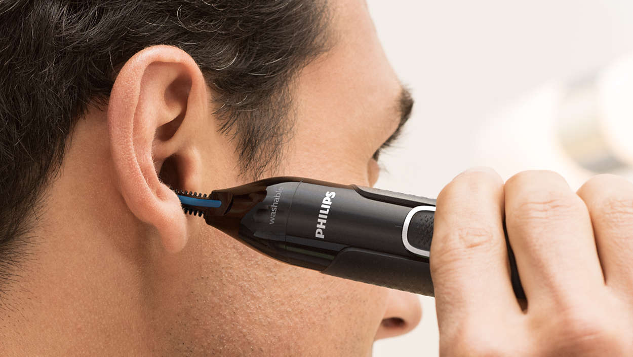 Een persoon die oorhaar trimt met een zwarte en blauwe Philips trimmer.