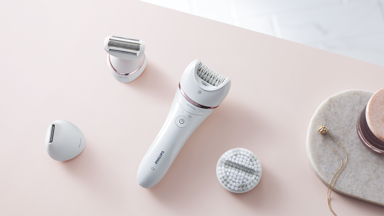 Witte en roségouden epilator en accessoires op roze oppervlak.