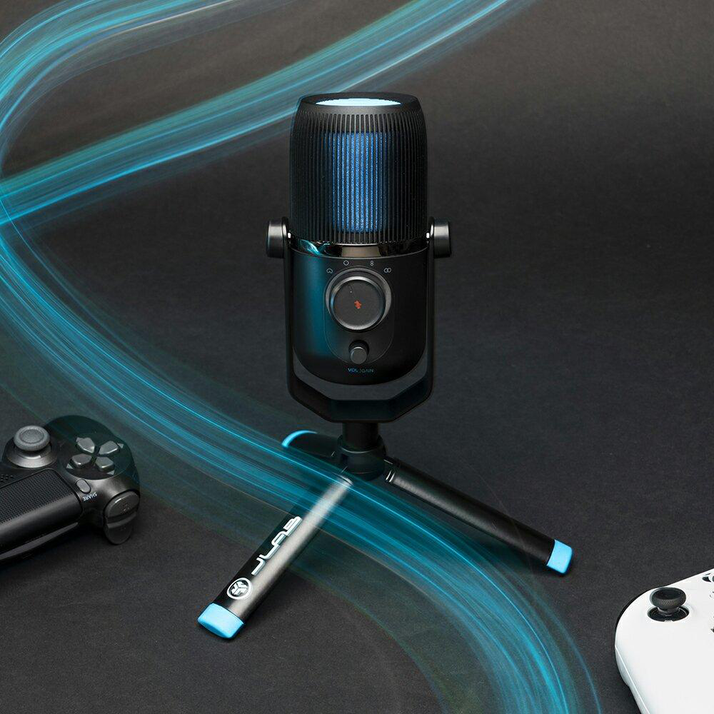 Schwarzes Mikrofon auf Stativ, blaue Lichter und zwei Gamecontroller im Hintergrund.