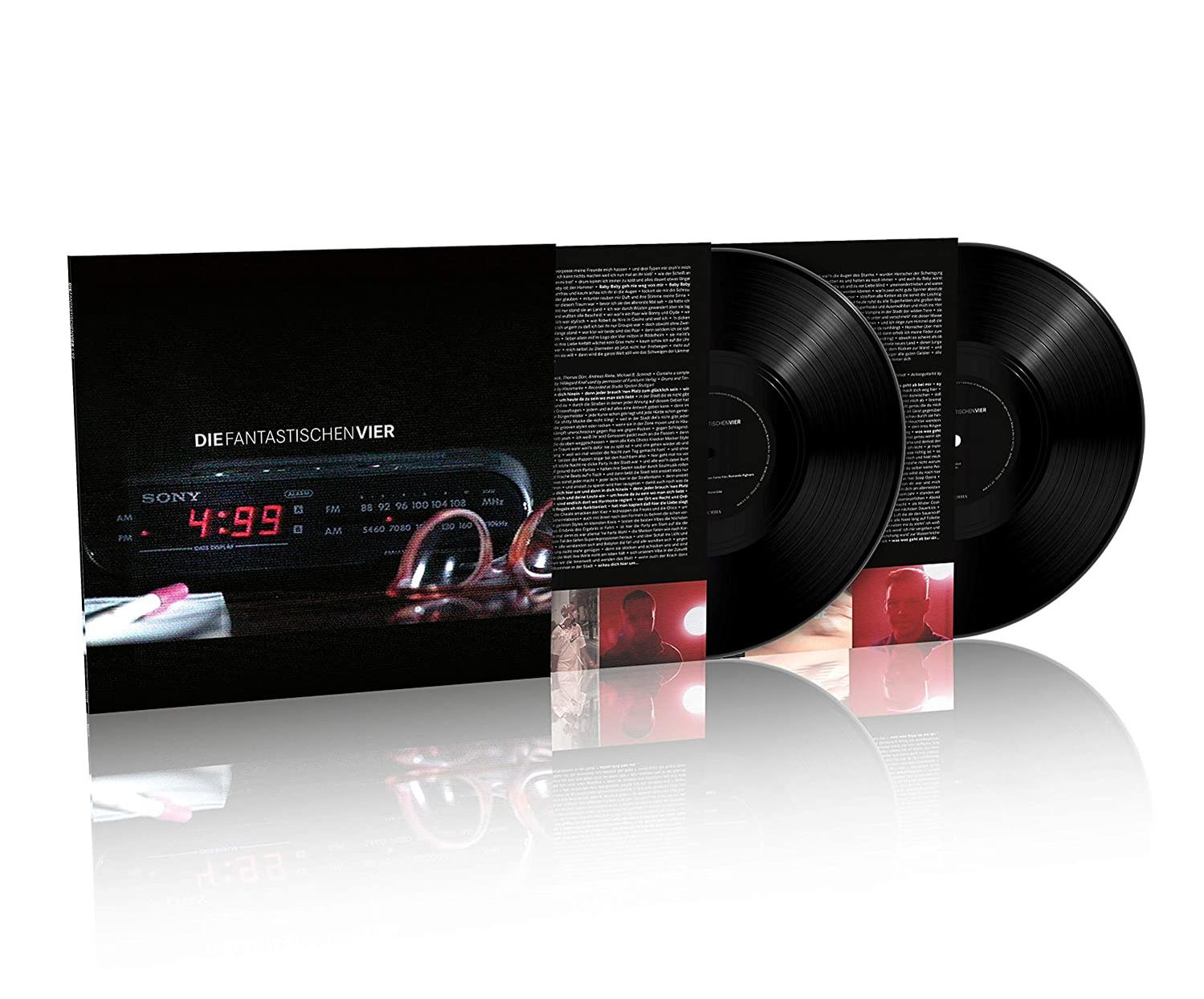 Drei Vinylplatten auf einem schwarzen Albumcover. Das Cover hat Text und ein Bild einer Uhr und einer Brille.