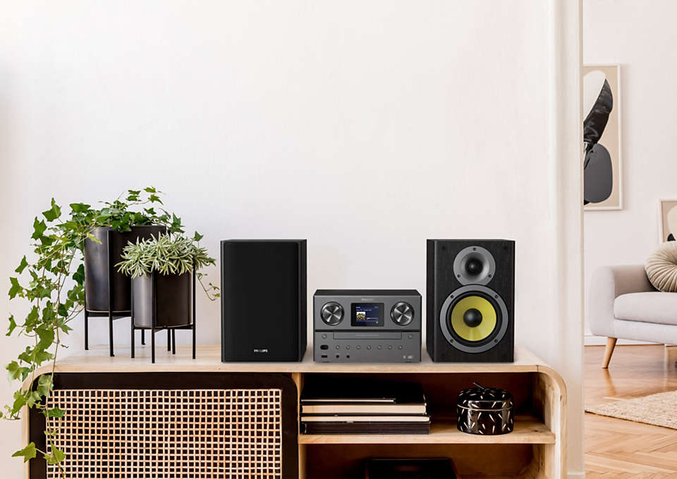 A modern audio system, with speakers, a receiver, and plants, on a wooden cabinet.