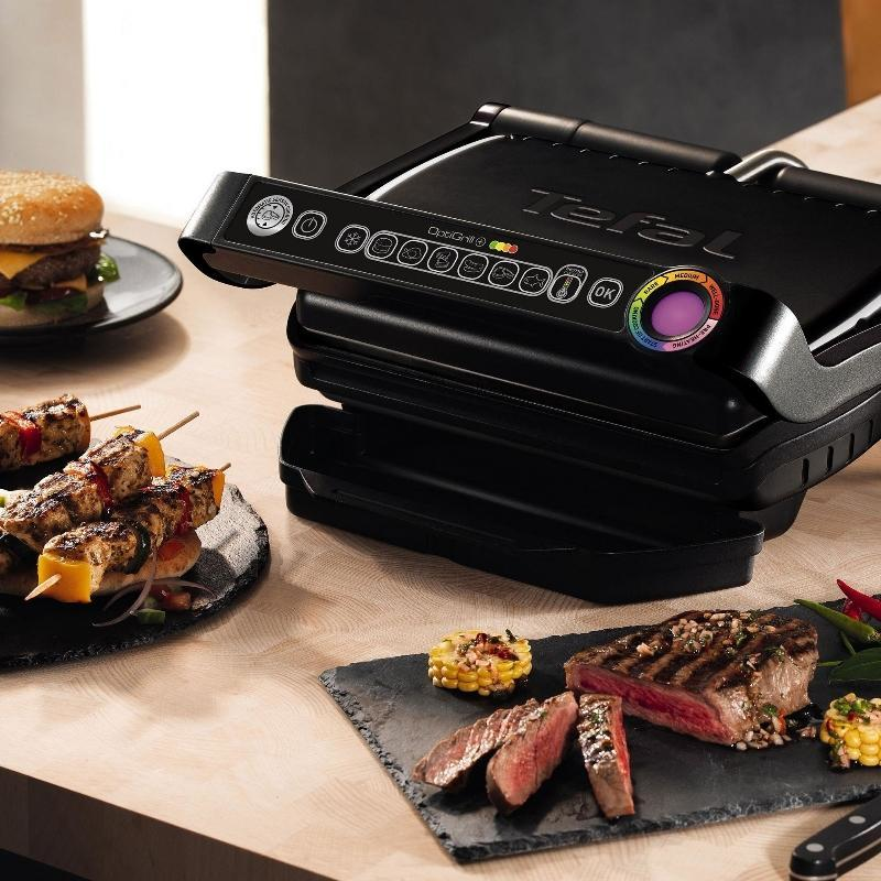 Fekete pultos grill ételekkel egy faasztalon. Steakek és nyársak vannak.