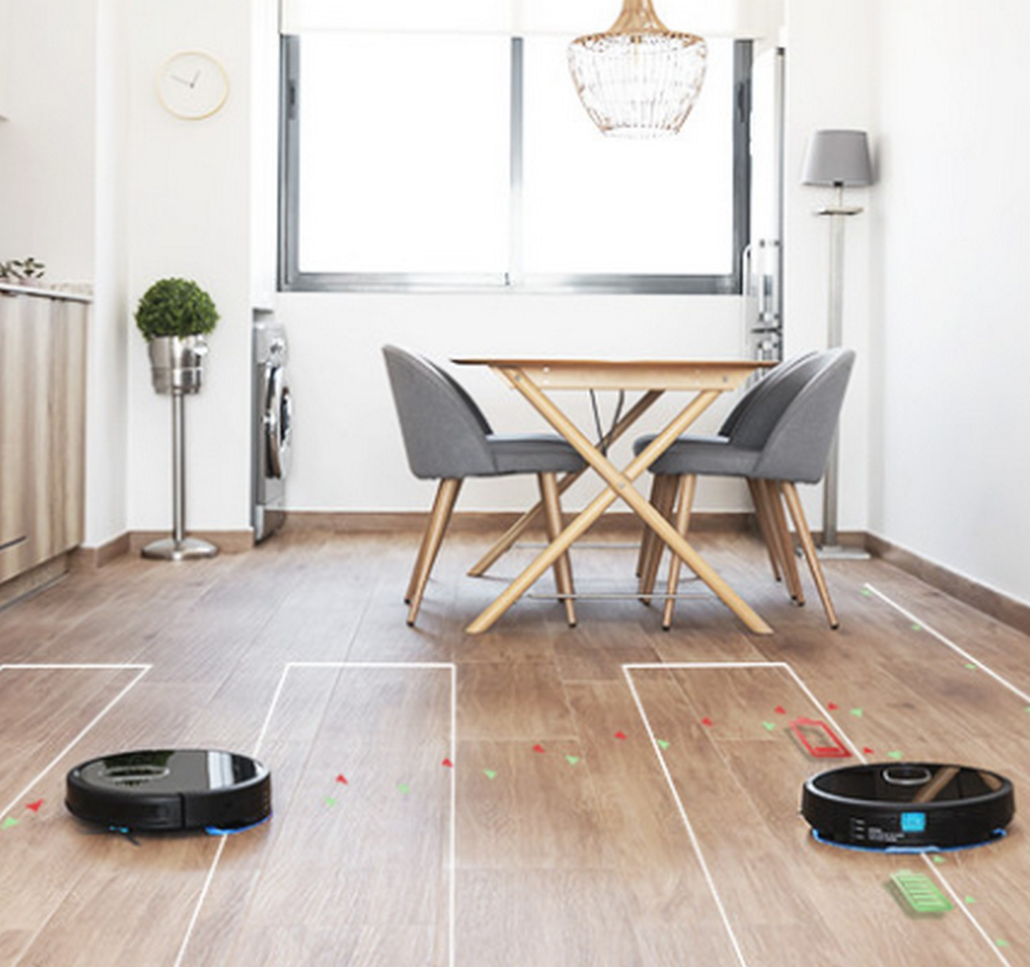 Dos aspiradoras robóticas limpiando un piso de madera con una mesa y sillas de fondo.