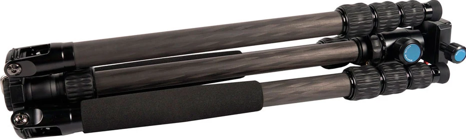 Un trépied plié noir et gris avec des pieds en fibre de carbone. Une poignée en mousse est sur la jambe centrale.