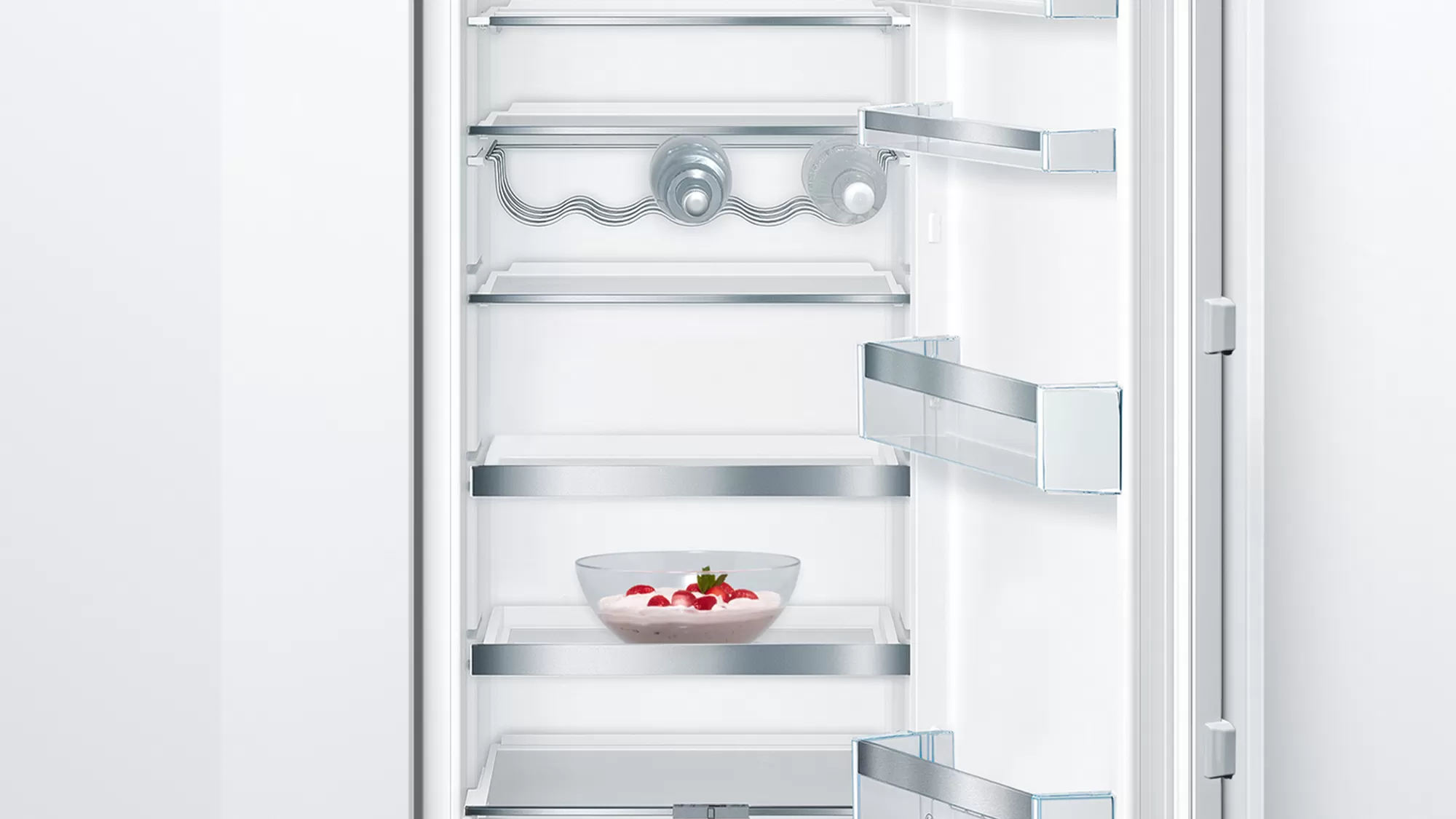 Réfrigérateur blanc ouvert avec des étagères, un bol de fraises et un porte-bouteilles.