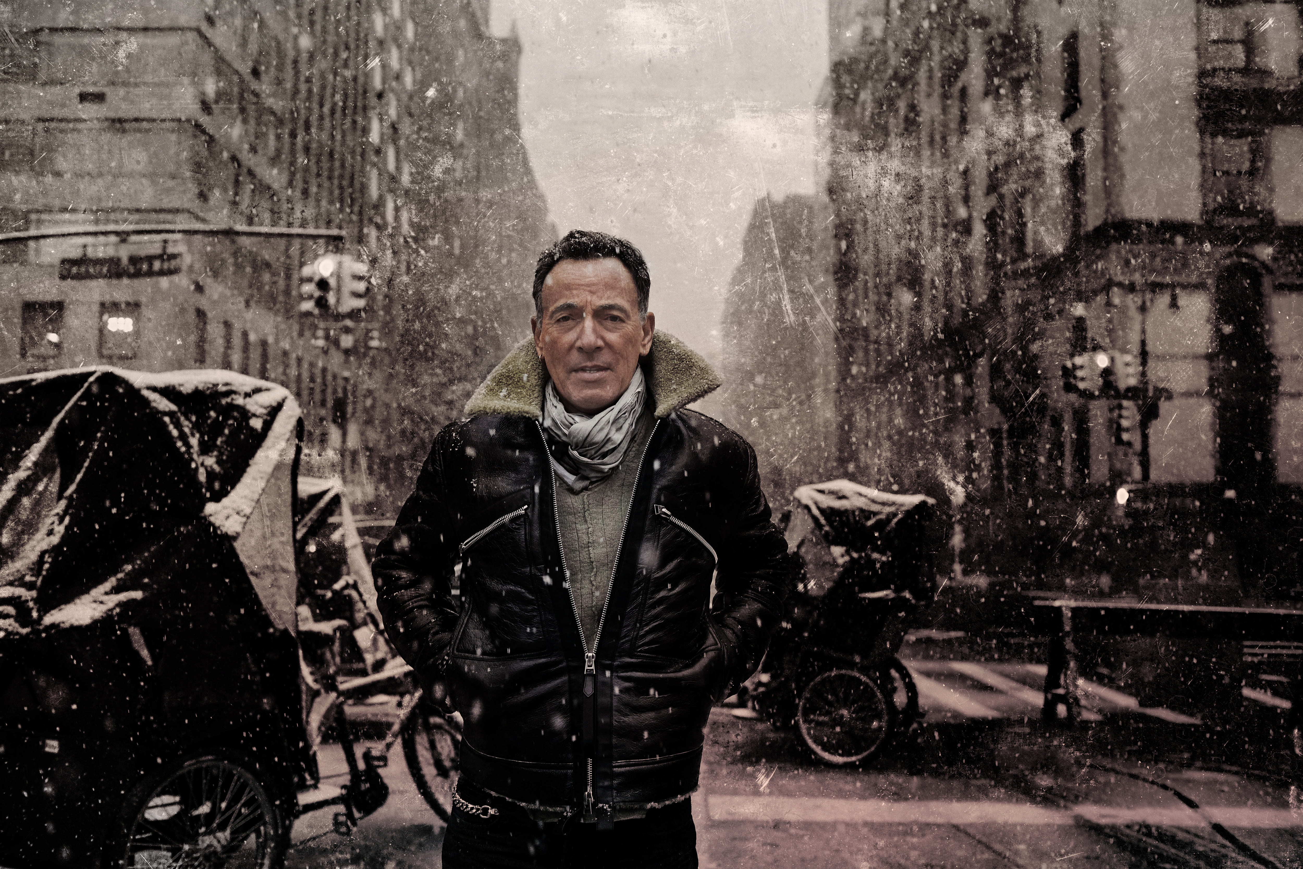 Bruce Springsteen in einer verschneiten Stadtszene mit schwarzer Jacke und Schal.