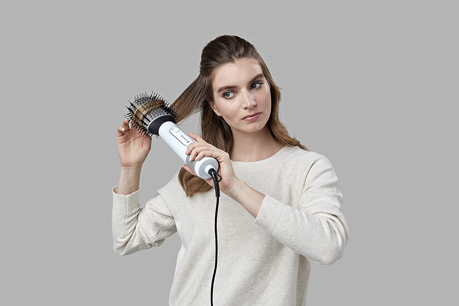 Frau benutzt eine Haarstylingbürste. Sie steht vor grauem Hintergrund.