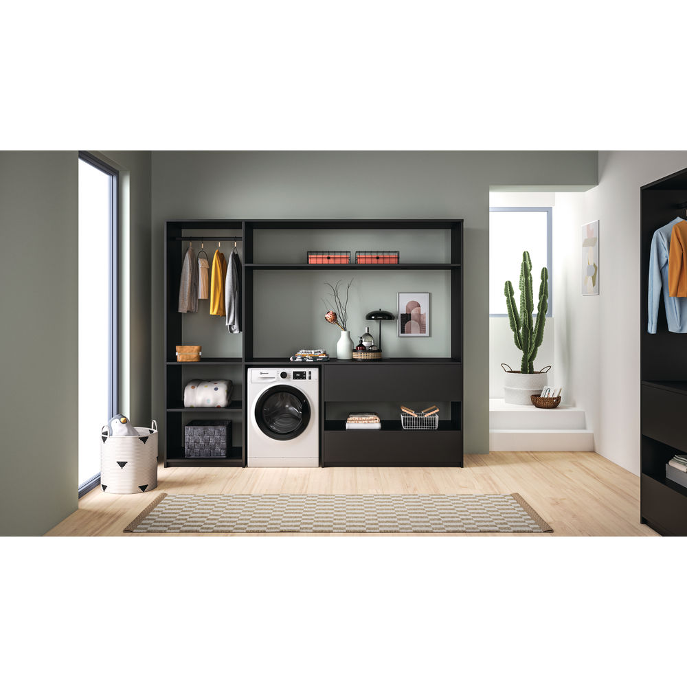 Waschküche mit schwarzen Schränken, Waschmaschine und Teppich. Kleidung hängt und ein Kaktus im Hintergrund.