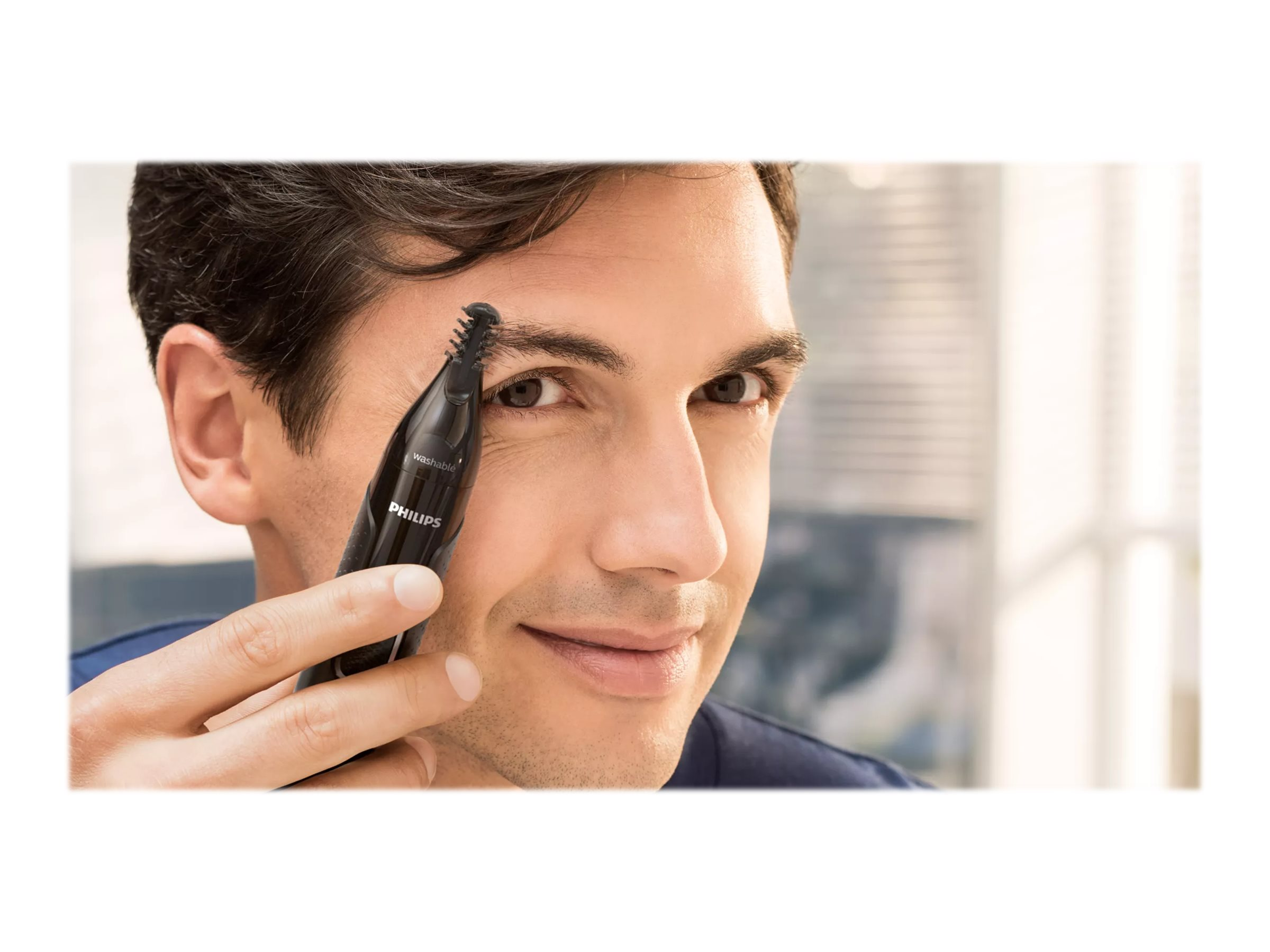 Mann benutzt einen schwarzen Philips-Trimmer, um seine Augenbraue zu trimmen. Weißer Hintergrund.
