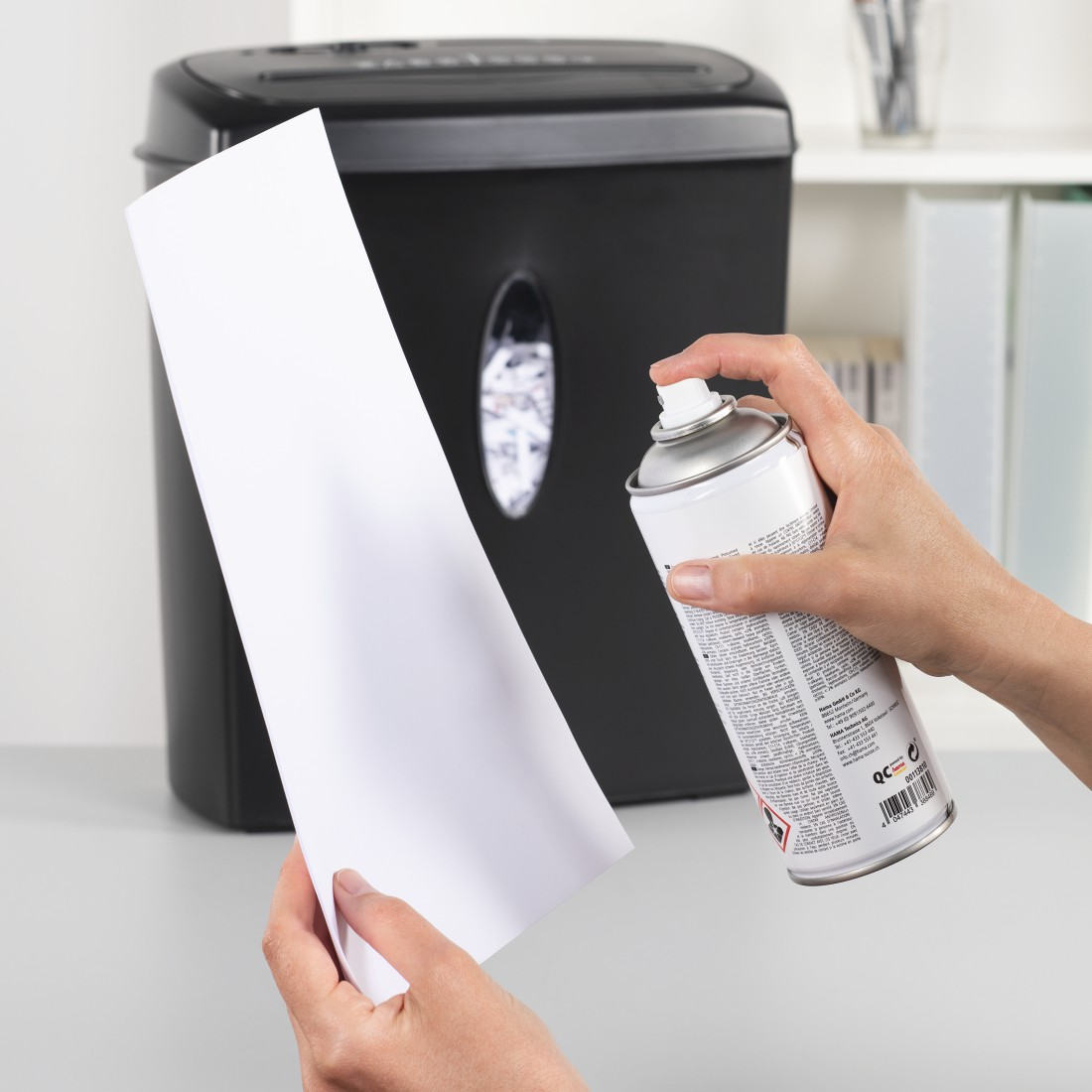 Person sprüht Papier in der Nähe eines Aktenvernichters, Büroumgebung, weißer Hintergrund.