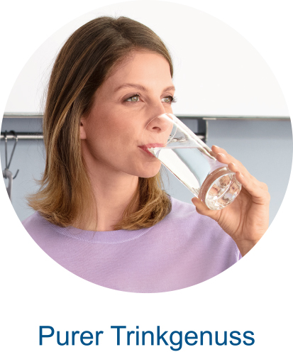 Une femme boit de l'eau dans un verre, en souriant à la caméra.