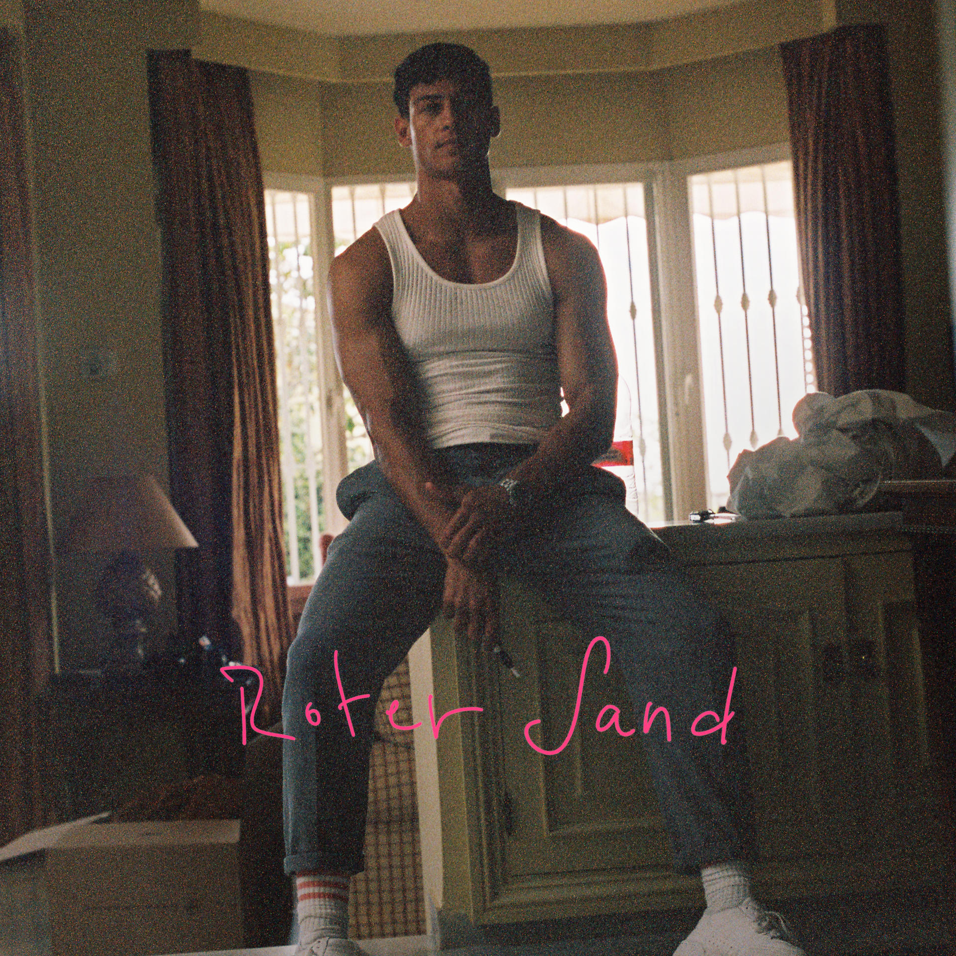 Mann in Tanktop, sitzend, Roter Sand Text, Innenraum.