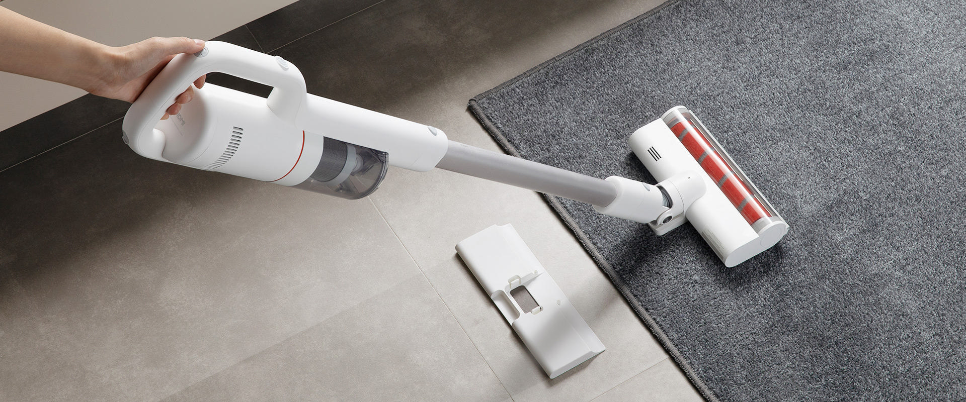 Ein weißer Handstaubsauger reinigt einen grauen Teppich.