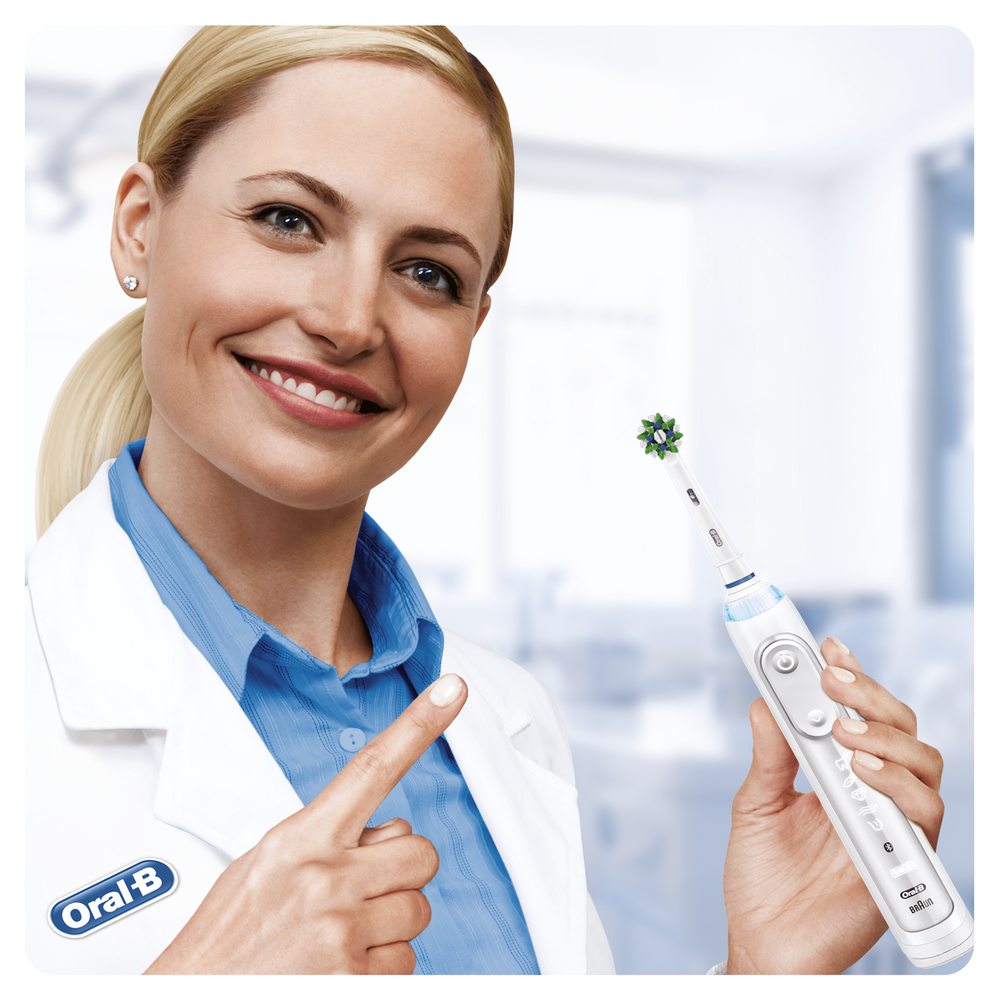 Una mujer sonriente con bata de laboratorio señala un cabezal de cepillo de dientes eléctrico.