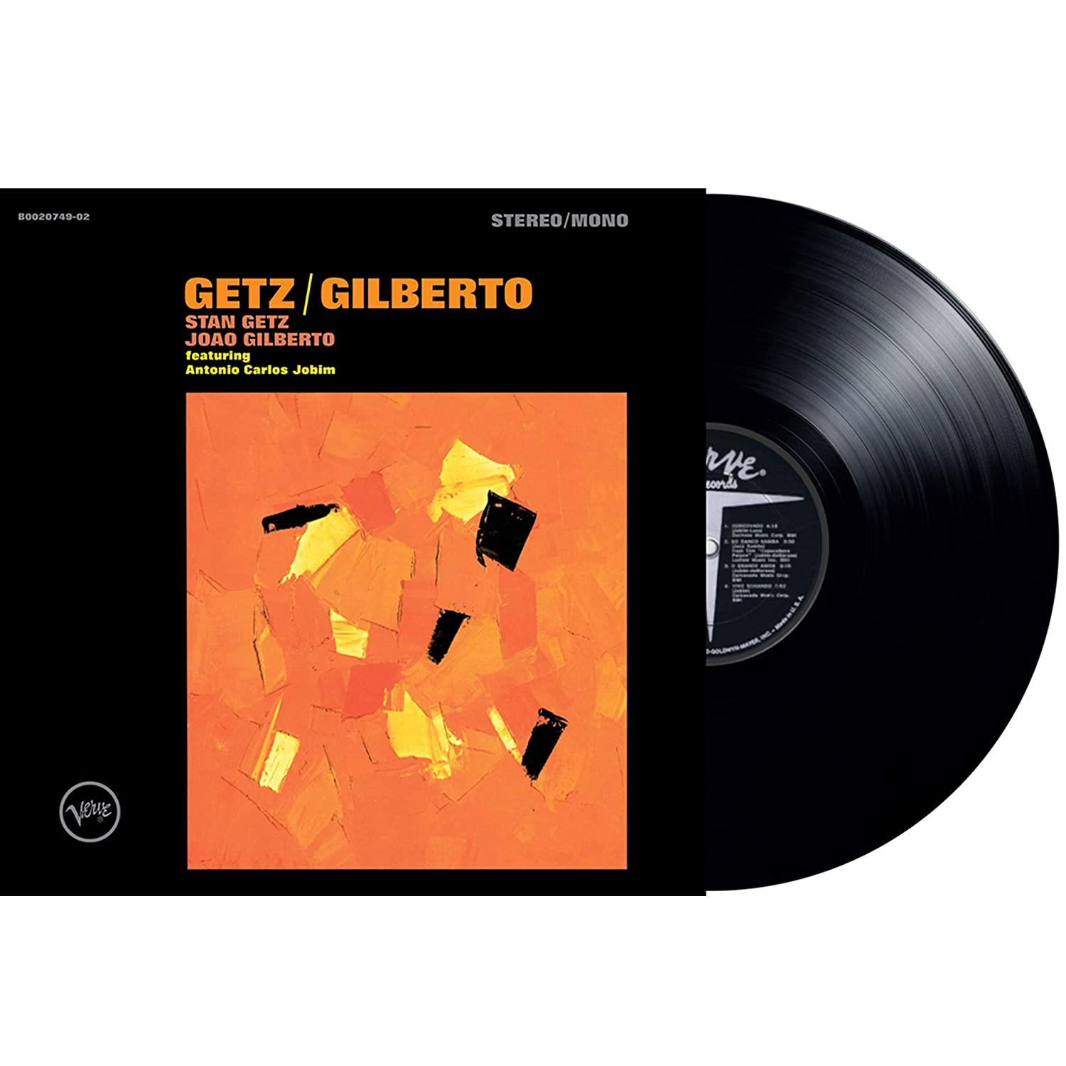 Egy bakelit lemez részben takar egy album borítót. A borító narancssárga, szöveggel és fekete. A lemez fekete, fehér címkékkel.