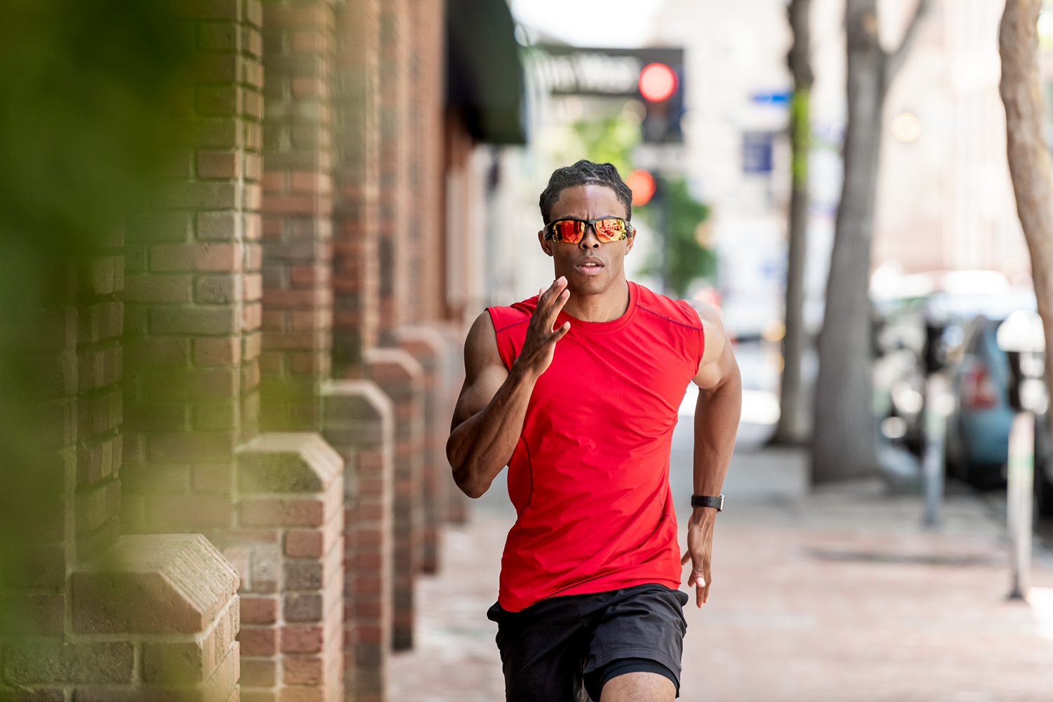 Man running towards the camera, wearing red shirt and sunglasses, in an urban setting.