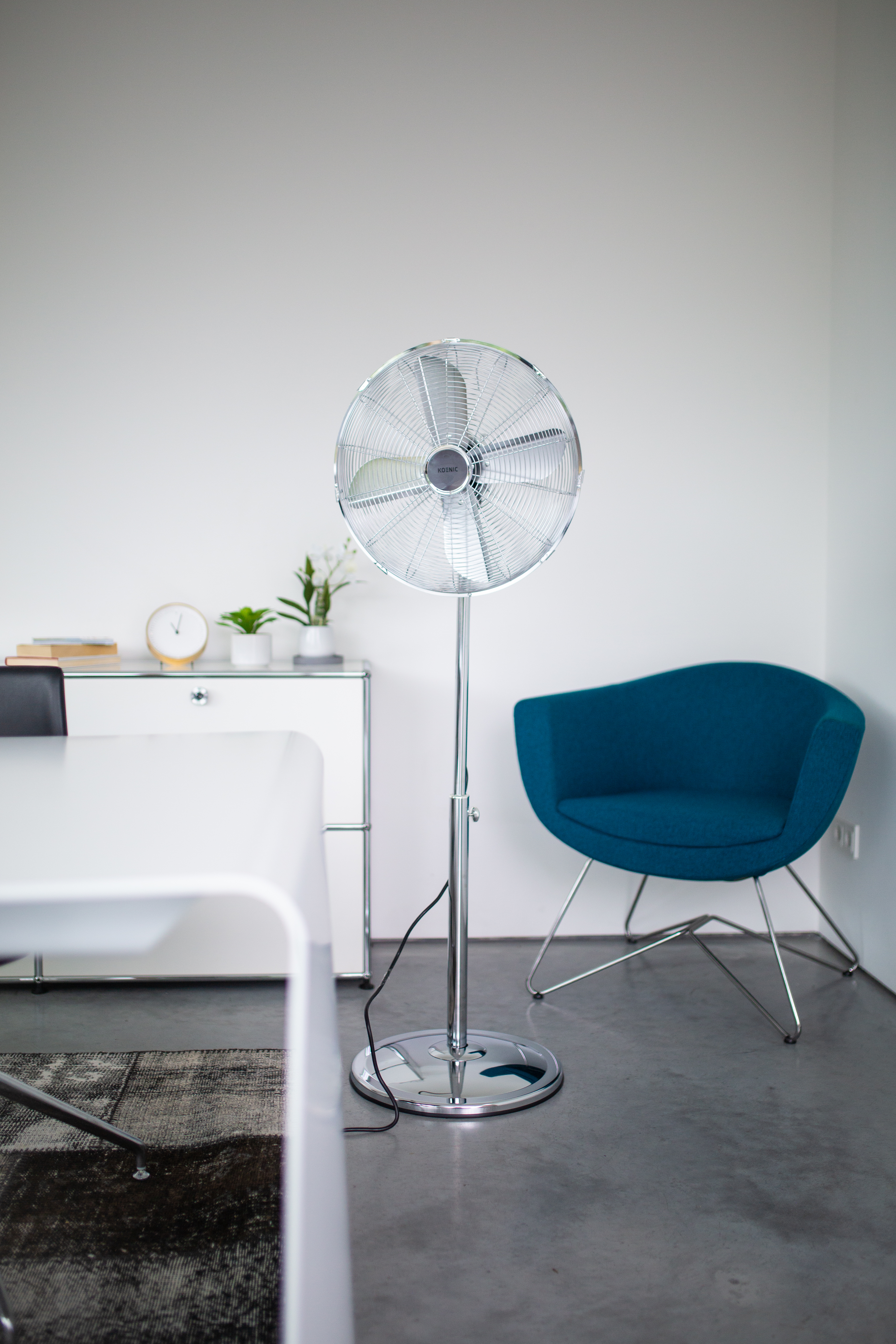 Un ventilatore da terra argentato è accanto a una poltrona blu.