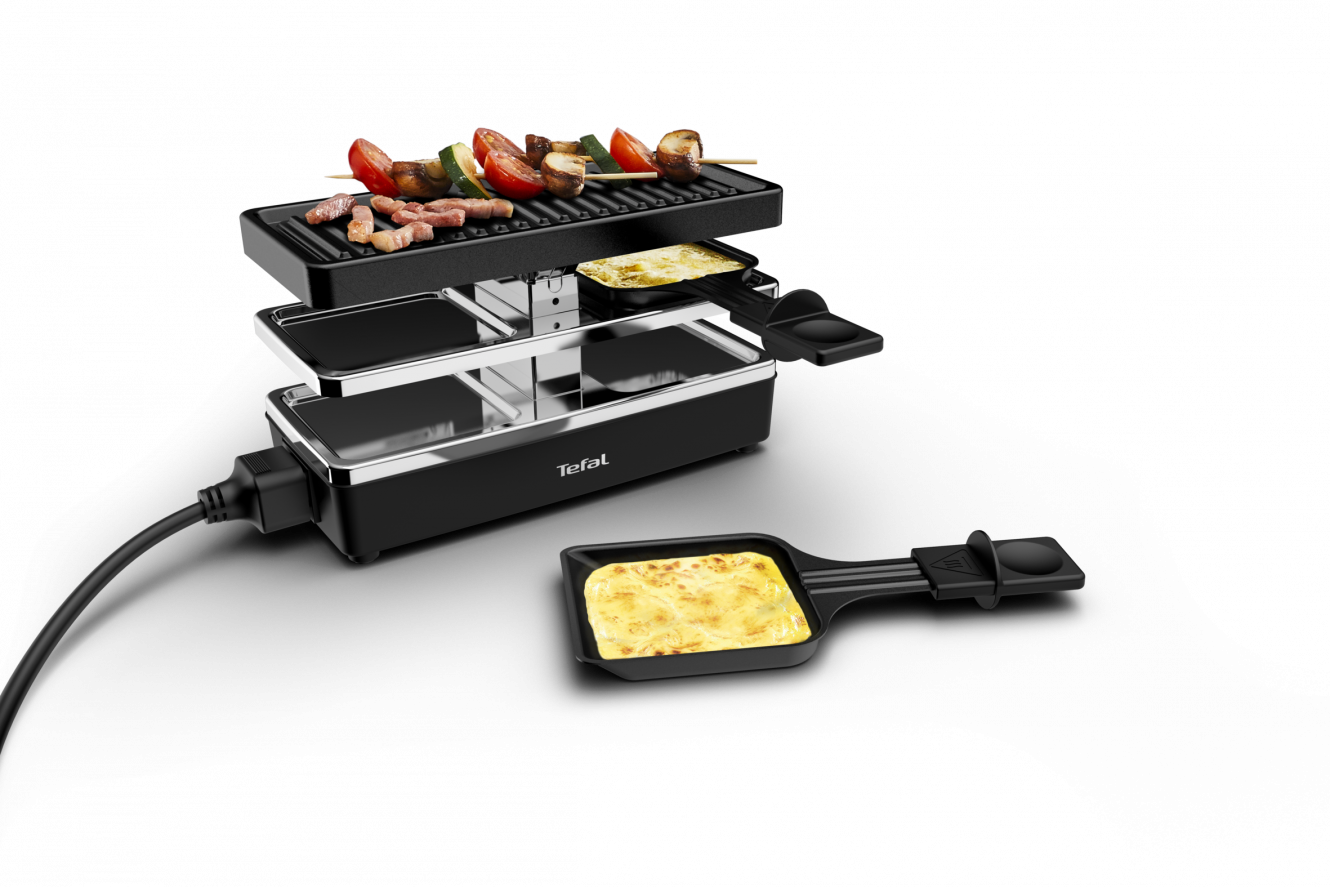 Grill à raclette avec de la nourriture dessus, et du fromage et des aliments cuits dans des poêles sur le comptoir.