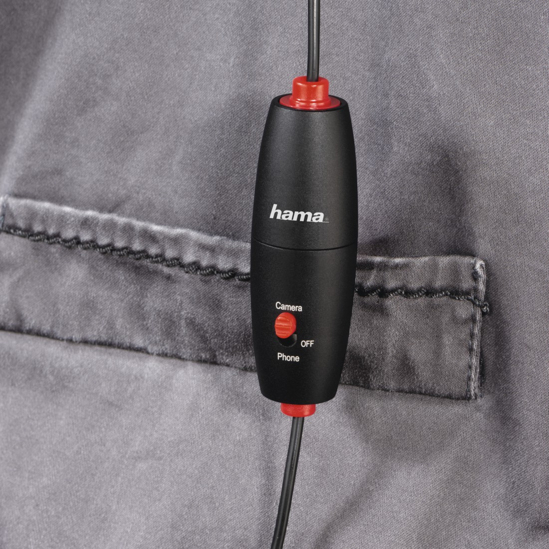 Ein schwarzes Gerät mit rotem Knopf an einer grauen Jacke befestigt. Das Wort 'hama' ist sichtbar.