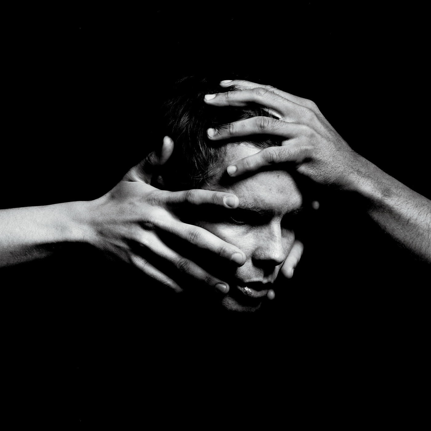 Photo en noir et blanc d'un homme dont le visage est couvert par deux mains.