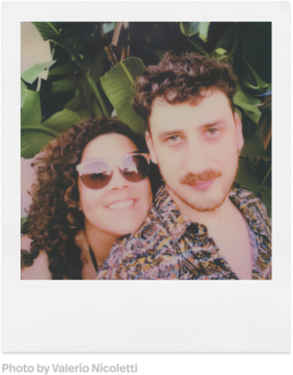 Foto im Polaroid-Stil eines lächelnden Paares, mit üppigem grünen Laub im Hintergrund.