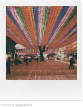 Polaroid-Foto einer Straße mit bunten Lichtern. Silhouetten von Menschen sind im Vordergrund zu sehen.