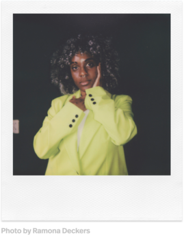Frau in neongrünem Blazer, Hände im Gesicht, blickt in die Kamera, vor dunklem Hintergrund. Polaroid-Stil.