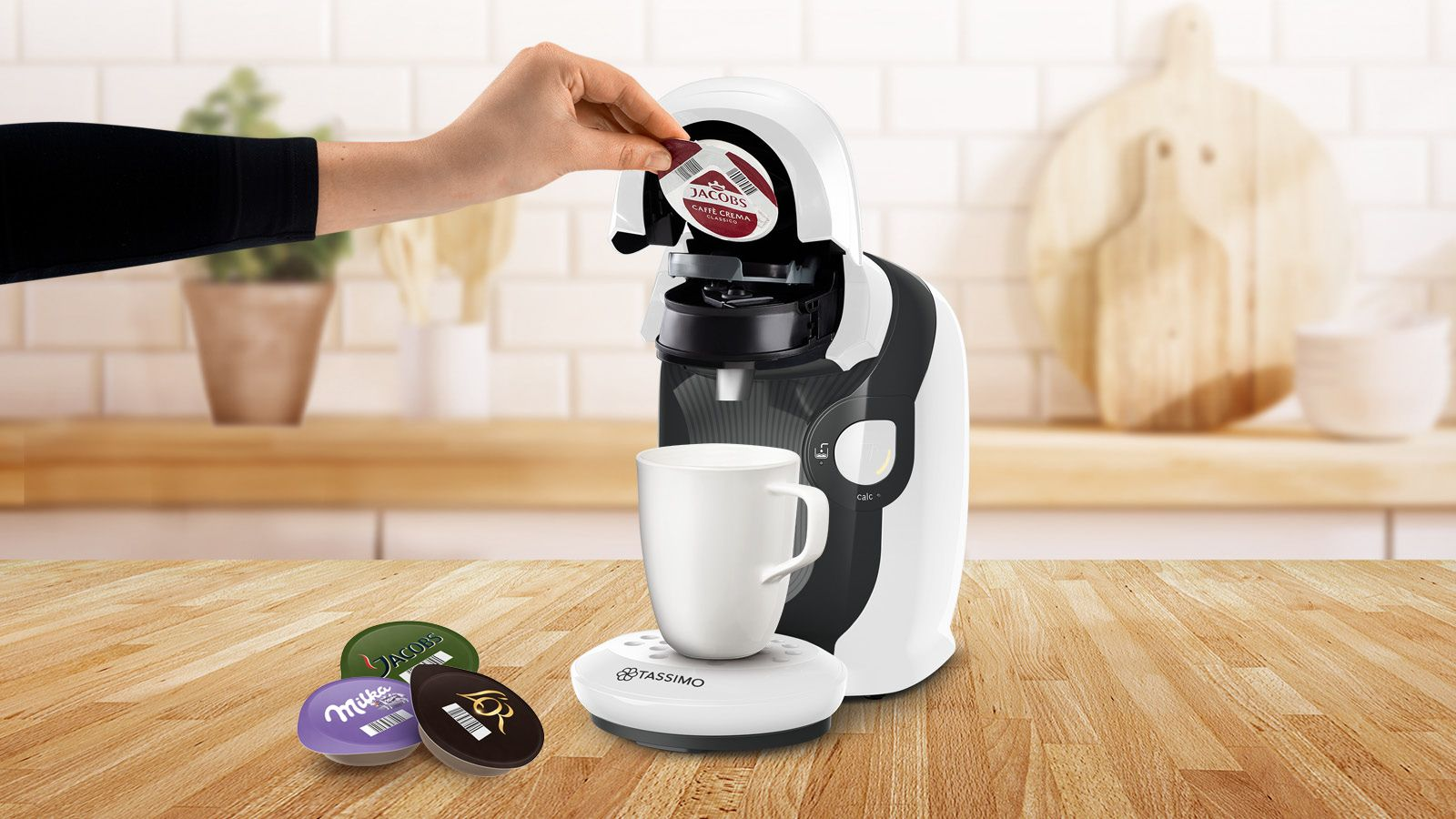 Person setzt einen Kaffee-Pod in eine Tassimo Kaffeemaschine ein.