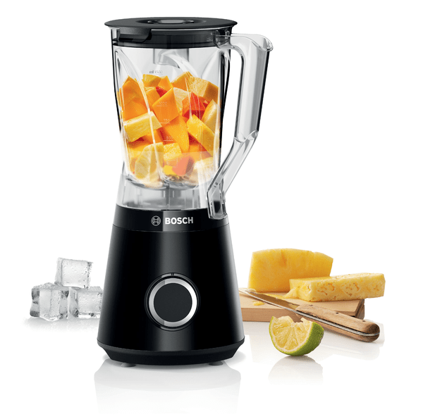 Schwarzer Bosch-Mixer mit gehackten Früchten, Eiswürfeln und einem Holzbrett mit Ananasscheiben.