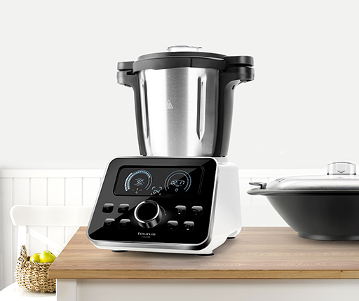 Electrodoméstico de cocina blanco y negro con pantalla digital y una olla encima, en una encimera de madera.