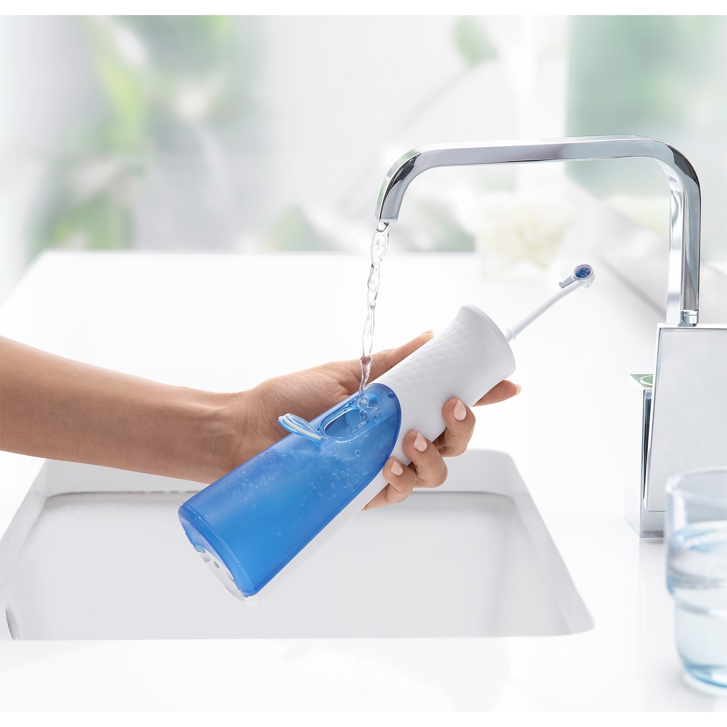 El, ağız duşunu dolduruyor. Su musluktan akıyor. Parlak bir banyoda beyaz lavabo.