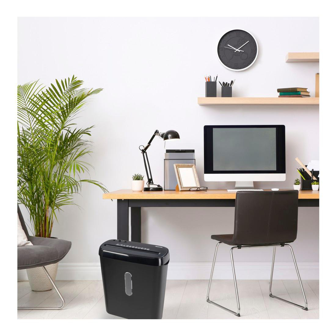 Büroinnenraum mit Schreibtisch, Aktenvernichter und anderem Büromaterial. Eine Pflanze und eine Uhr sind ebenfalls vorhanden.